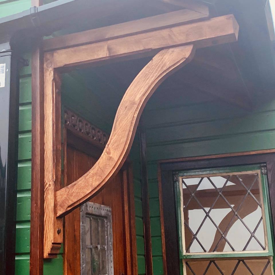 Snake style gallows bracket with a dark stain, used as a decorative feature on an outbuilding painted in a mid shade of green.